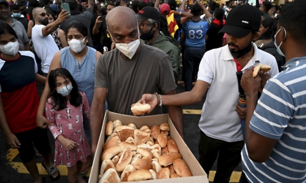 Một người đàn ông phát bánh mỳ cho đám đông tham gia biểu tình bên ngoài văn phòng Tổng thống Sri Lanka ở Colombo hôm 10/4. Ảnh: AFP.